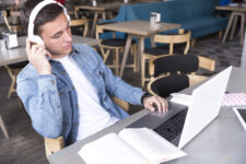 teenage-student-headphones-sitting-with-notebook-table